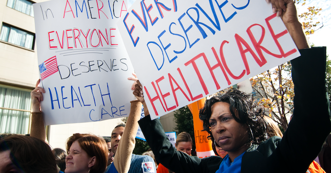 Two women at protest holding signs that say everyone deserves health care